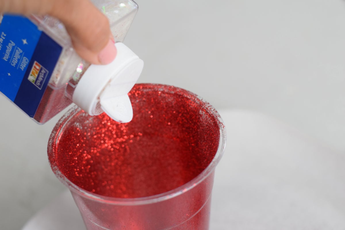 pouring glitter into clear cup for Uncle Sam hat craft 