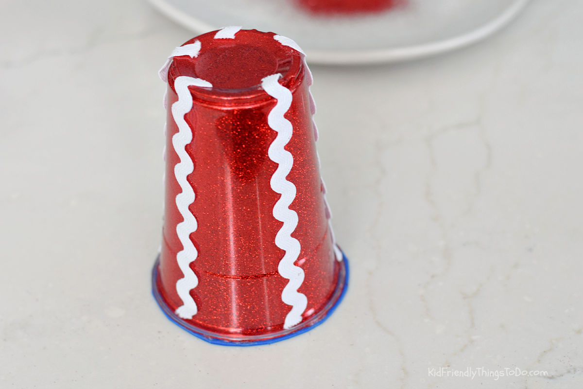 gluing white rickrack onto glittered cup for Uncle Sam hat craft
