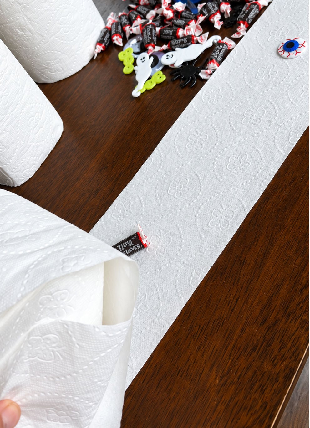 Candy and small Halloween prizes spaced along toilet paper while making the mummy prize ball
