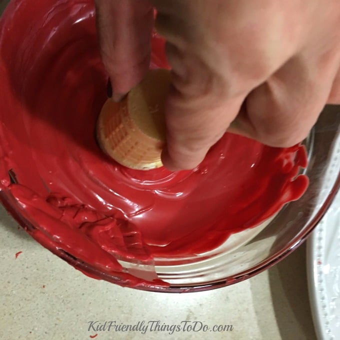 dipping a cake cone into a bowl of melted red candy melts