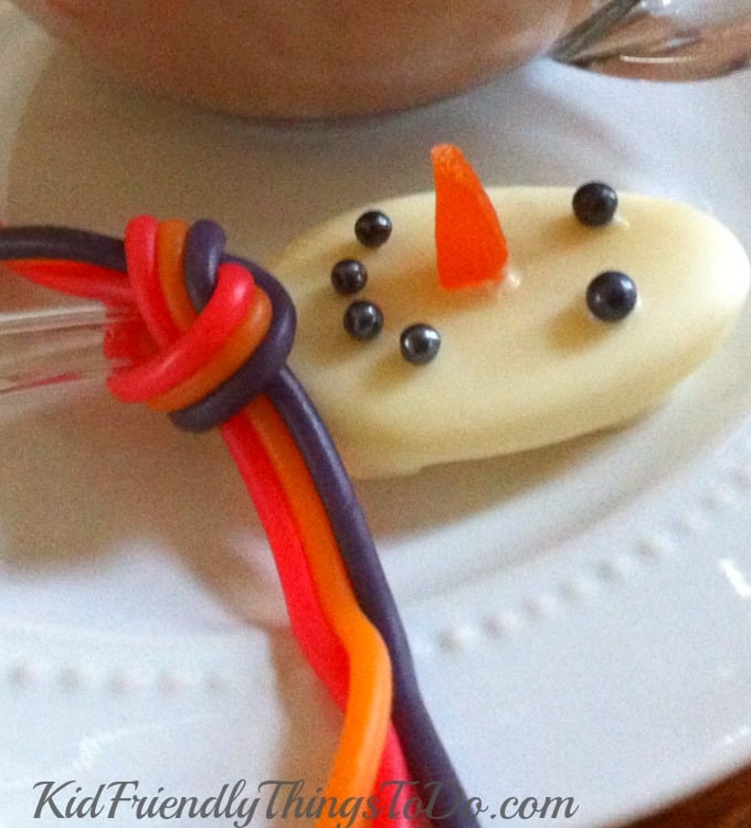 white chocolate-dipped spoon decorated like a snowman with black sugar pearls, an orange slice nose, and colored licorice scarf. 