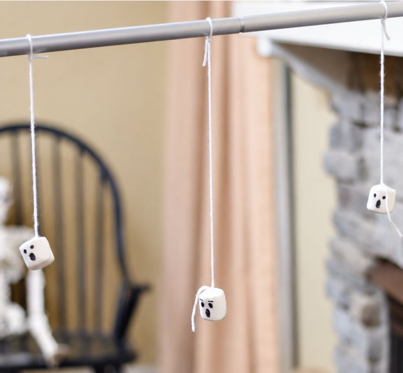  Ghost-face marshmallows hanging from strings tied to a broomstick.