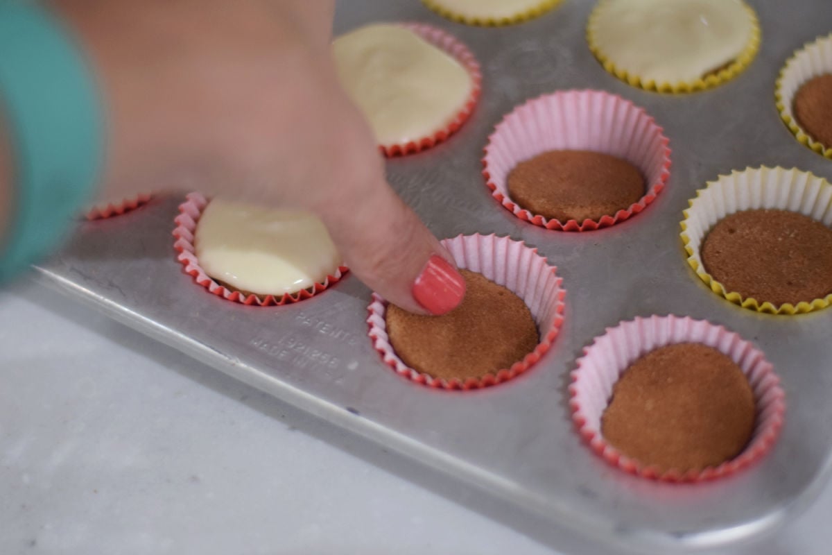 Placing a whole vanilla wafer into a mini cupcake liner in a muffin pan.