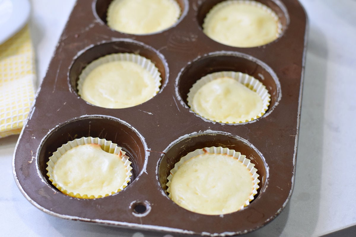 Baked mini cheesecakes in yellow mini cupcake liners inside a regular-sized muffin pan.