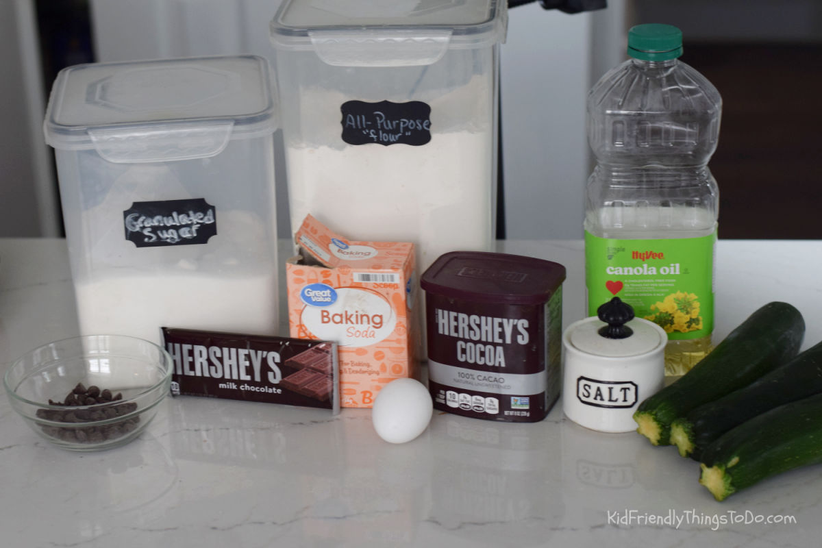 Ingredients for zucchini brownies including grated zucchini cocoa chocolate chips flour sugar oil and Hershey chocolate