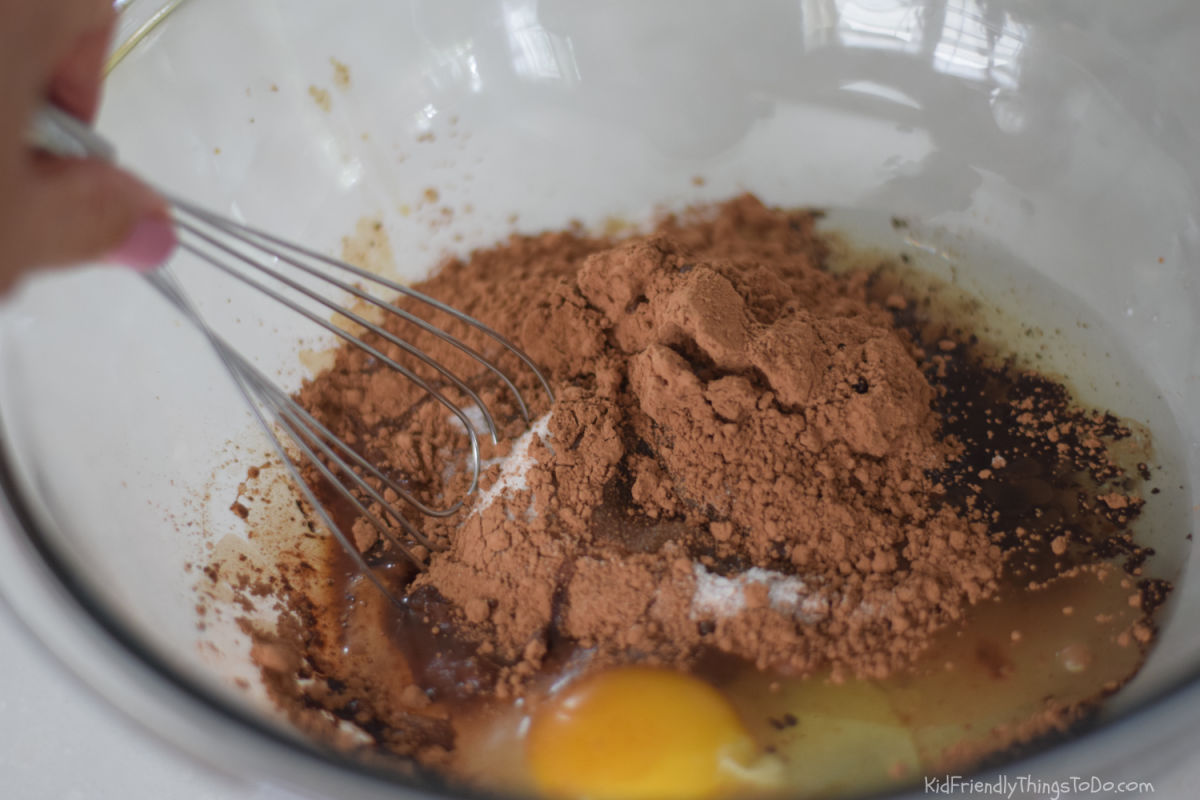 Sugar oil egg cocoa and vanilla being mixed for zucchini brownies