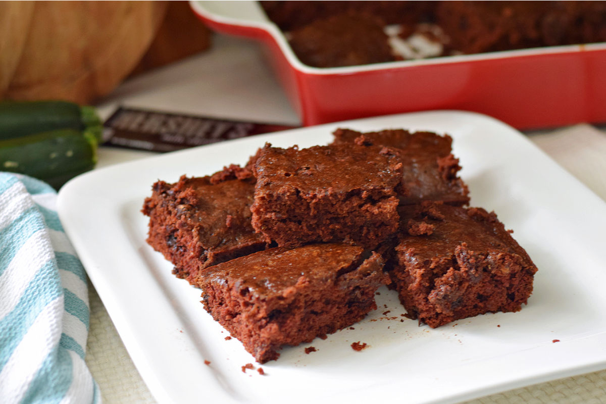 Chocolate zucchini brownies with chocolate chips and chocolate chunks stacked on a white plate.