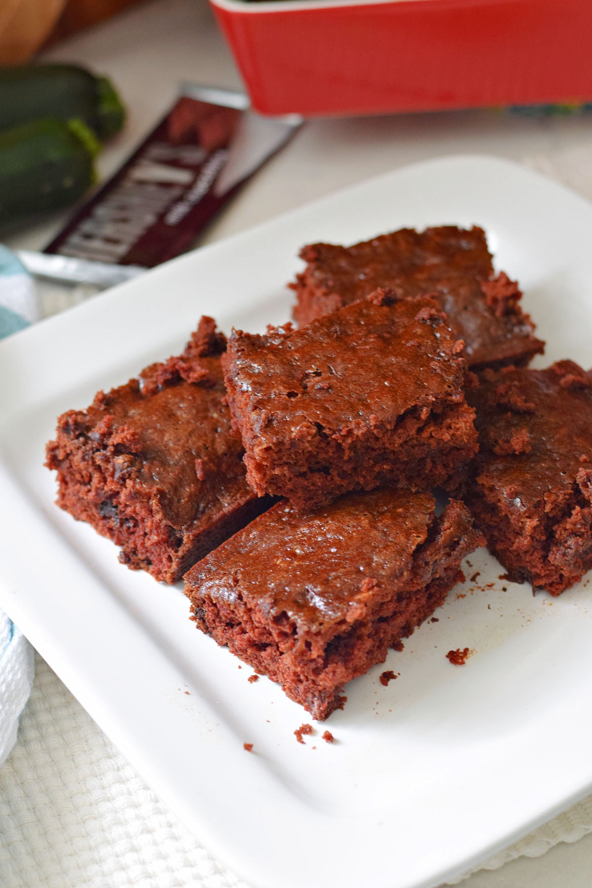 Chocolate zucchini brownies with chocolate chips and chocolate chunks stacked on a white plate.