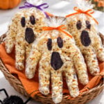 Popcorn-filled glove ghosts with black faces and orange and purple ribbon bows displayed in a woven basket beside a fuzzy black spider.