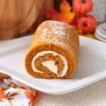 Homemade pumpkin roll dusted with powdered sugar, with a cream cheese swirl visible at the cut end.