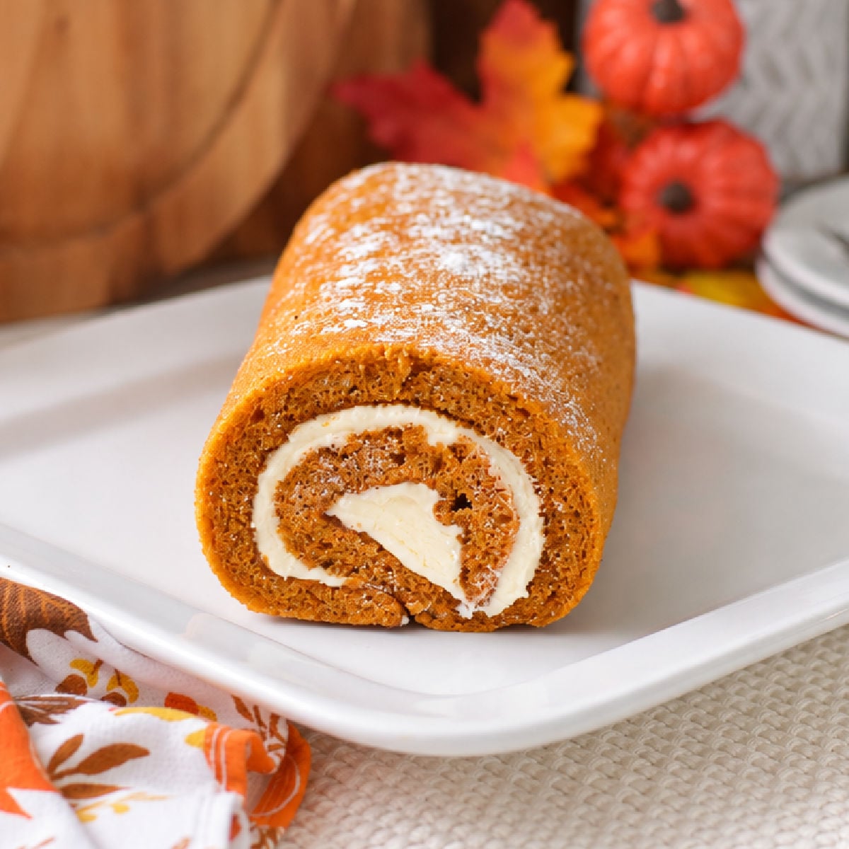 Homemade pumpkin roll dusted with powdered sugar, with a cream cheese swirl visible at the cut end.