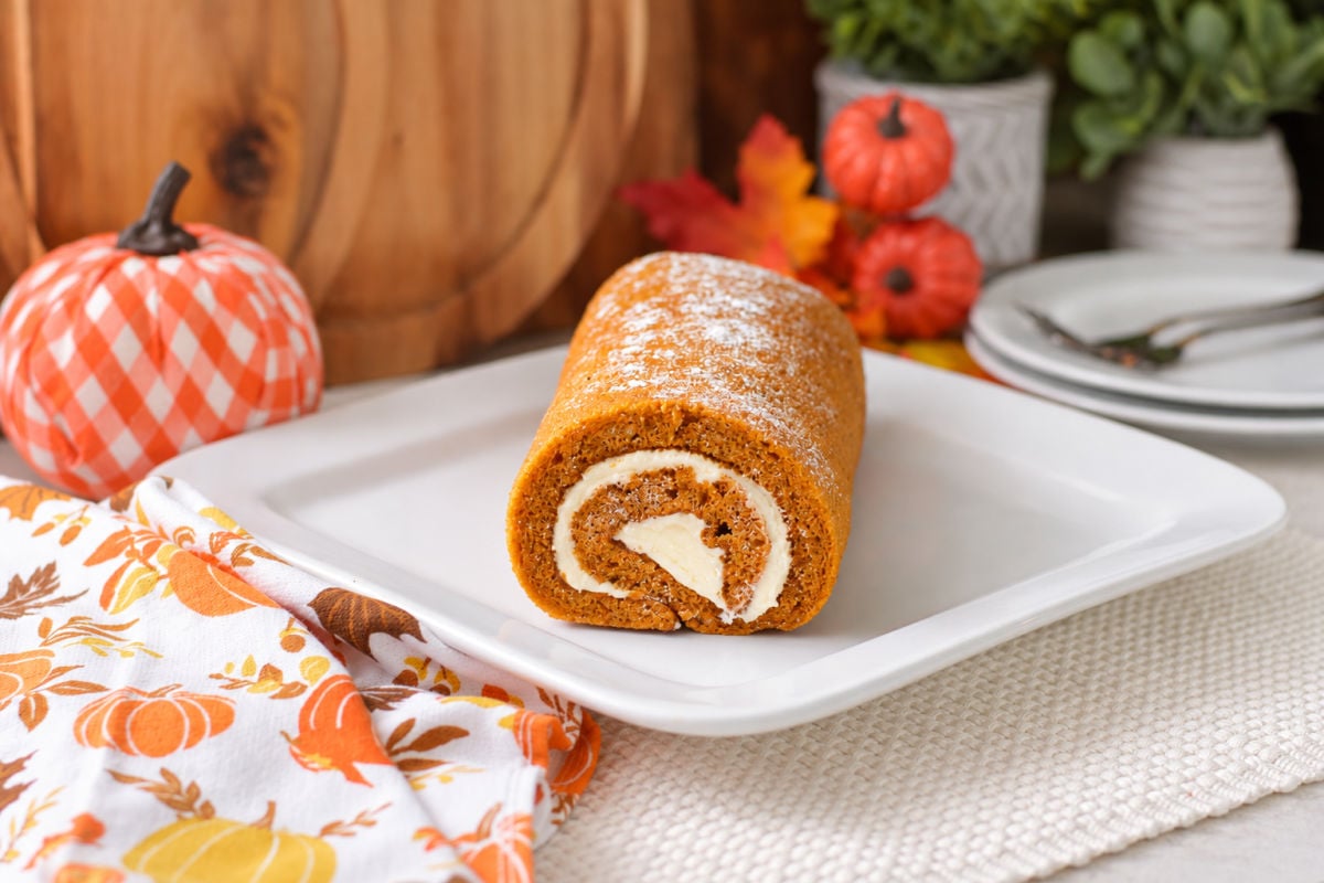 Homemade pumpkin roll dusted with powdered sugar, with a cream cheese swirl visible at the cut end.