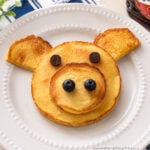 Pig pancakes made with pancake batter, chocolate chip eyes, and blueberry nostrils served on a white plate for a fun kids breakfast idea