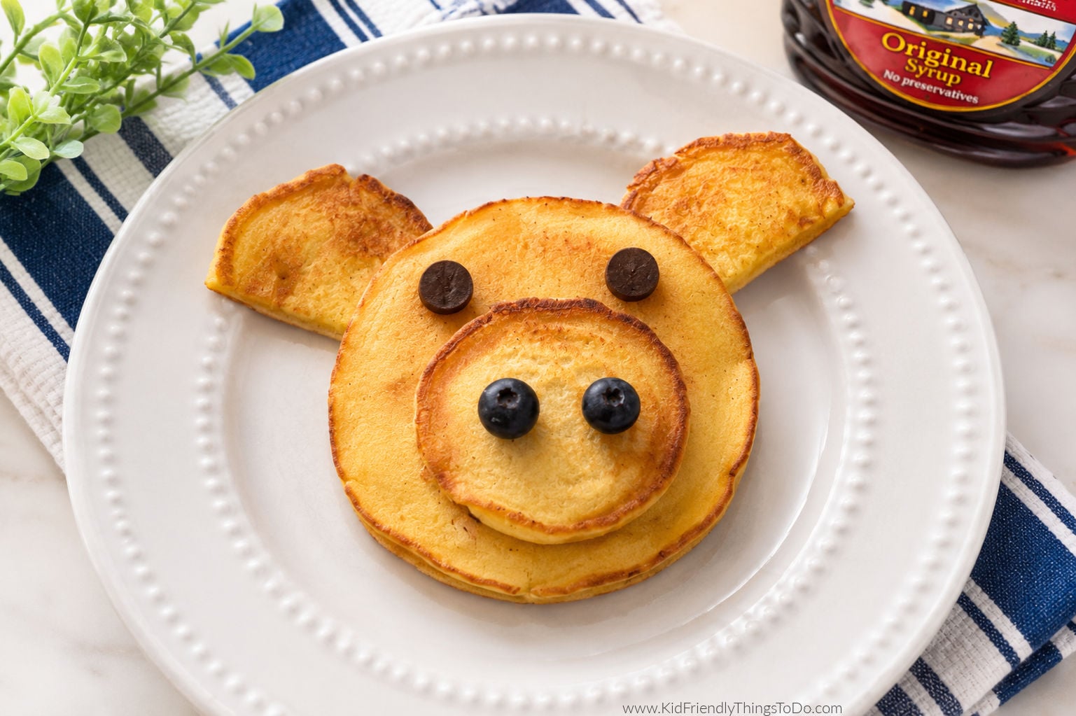 Pig pancakes made with pancake batter, chocolate chip eyes, and blueberry nostrils served on a white plate for a fun kids breakfast idea
