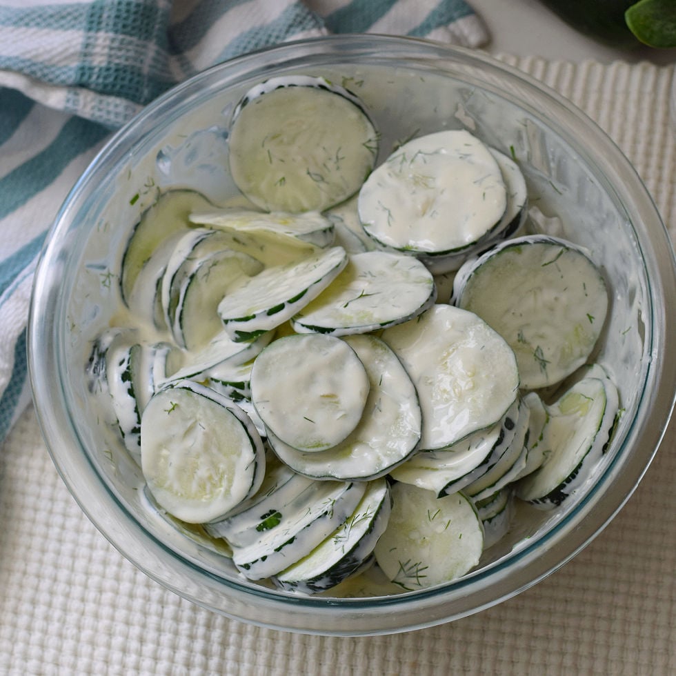 Creamy cucumber salad with skin-on cucumber slices coated in sour cream, mayo, and dill dressing in a clear glass bowl.