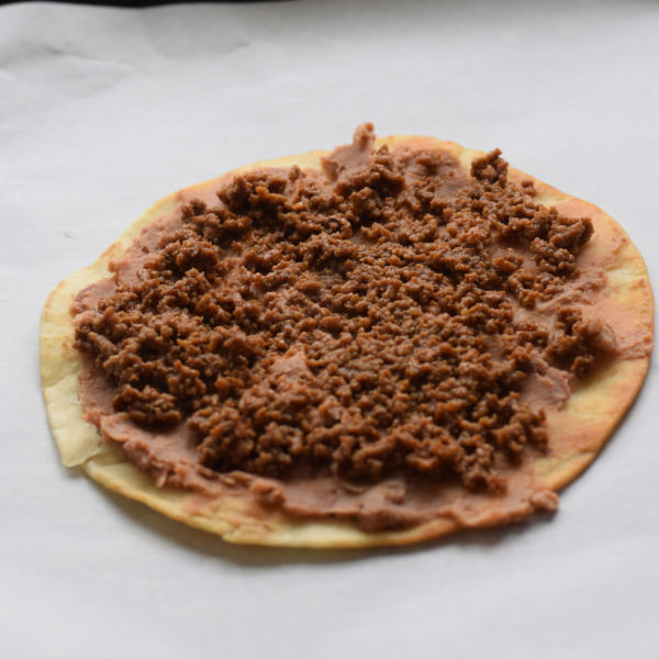 making a Mexican pizza - tortilla shell with refried beans and beef