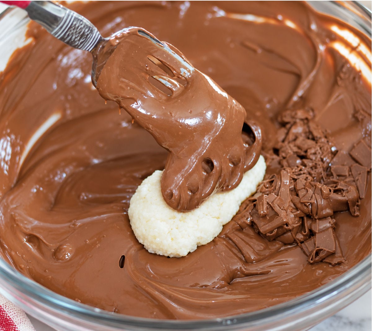 Coconut center being dipped in melted chocolate for a homemade Mounds bar recipe