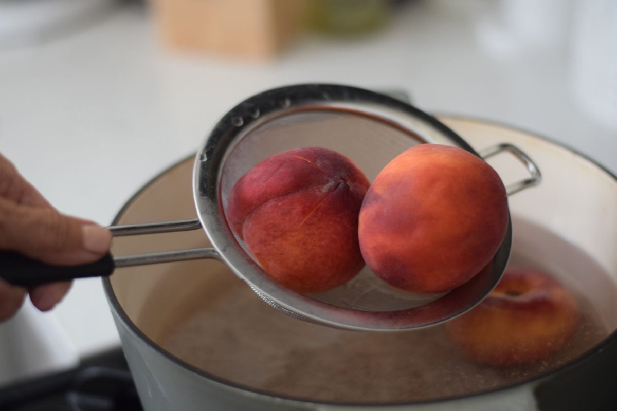 placing peaches in a pot of boiling water 
