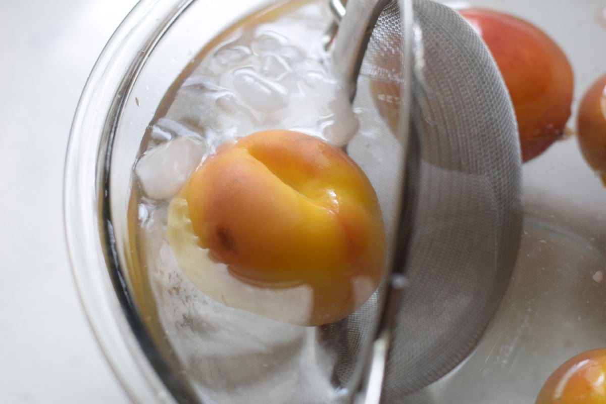 placing boiled peaches into a bath of ice water 