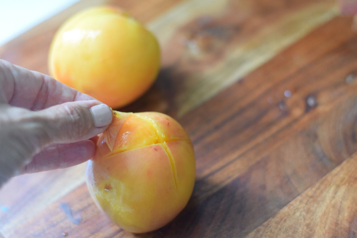 peeling skin from fresh peaches that have been scored, boiled and blanched 