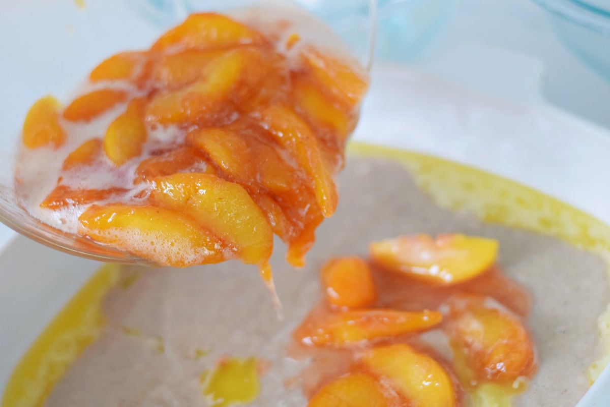 spooning fresh peaches over cobbler batter 