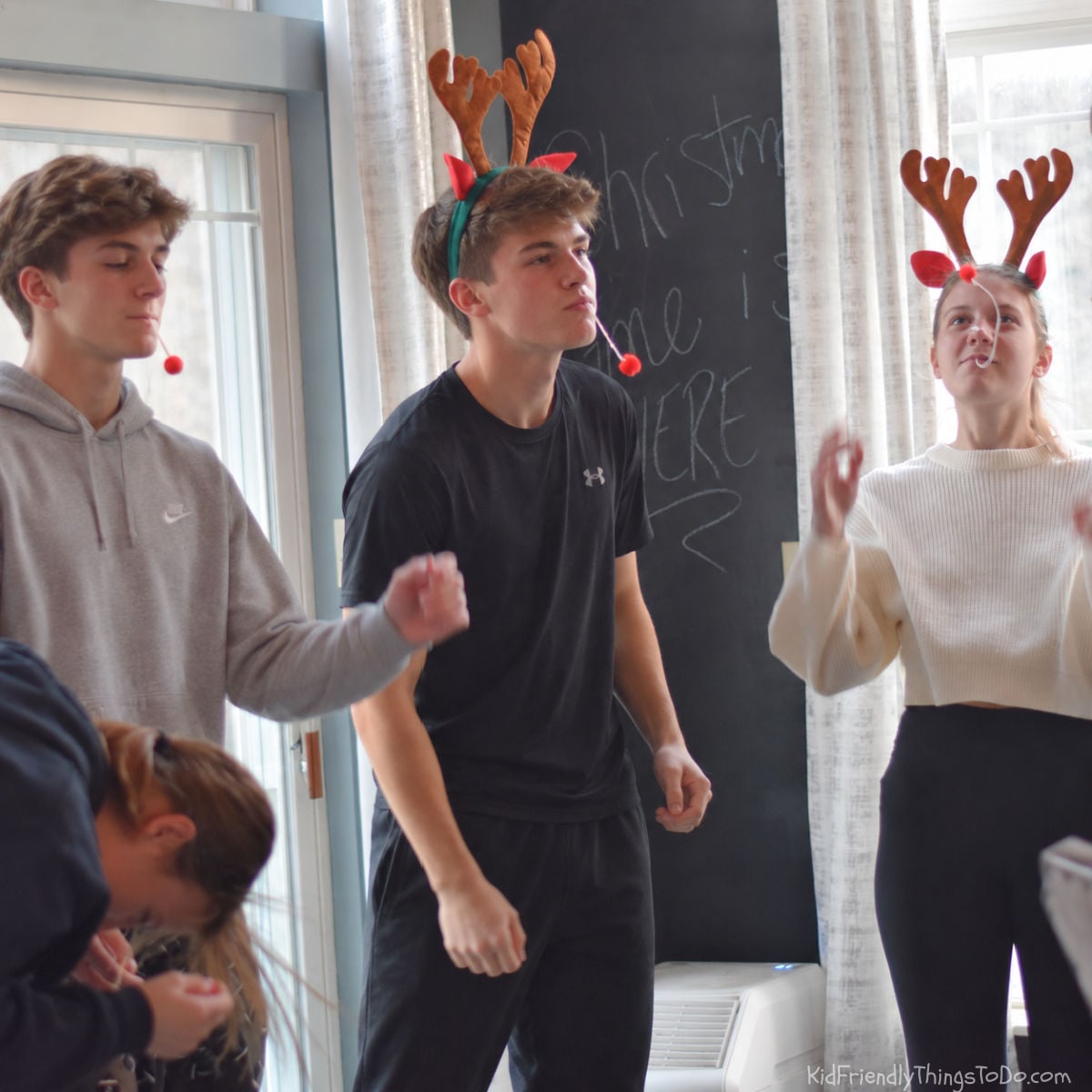 Teens playing Reindeer Nose Dive with red pom-poms and antler headbands for a Christmas Minute to Win It game.