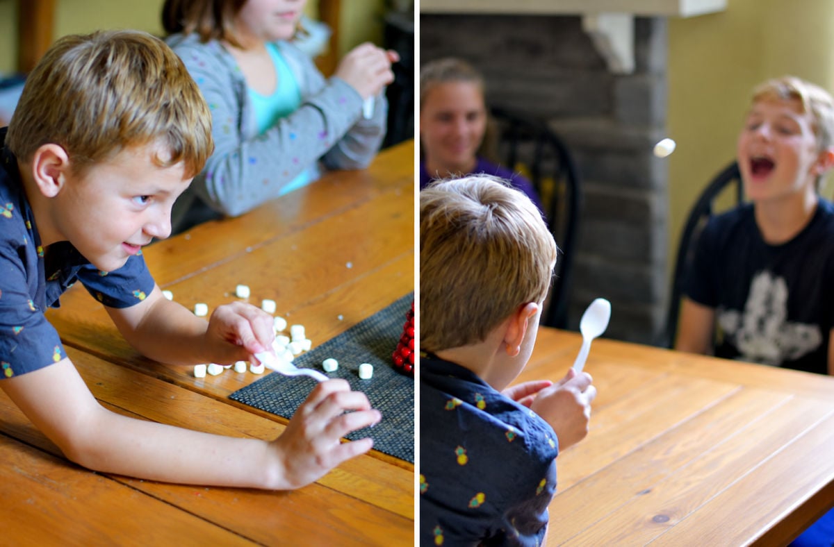 Kids playing Snowball Fight by tossing marshmallows with a spoon for a Christmas Minute to Win It game.