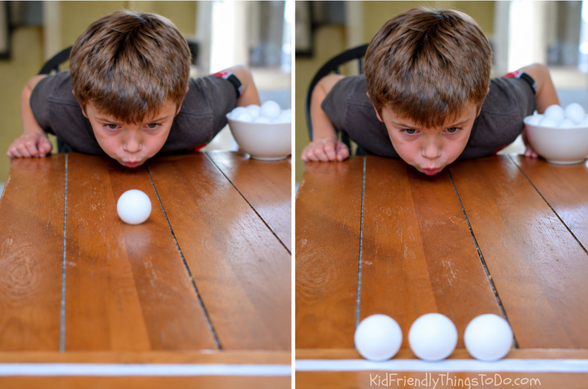 Boy blowing ping pong balls across a table for a Christmas Minute to Win It Build a Snowman game.