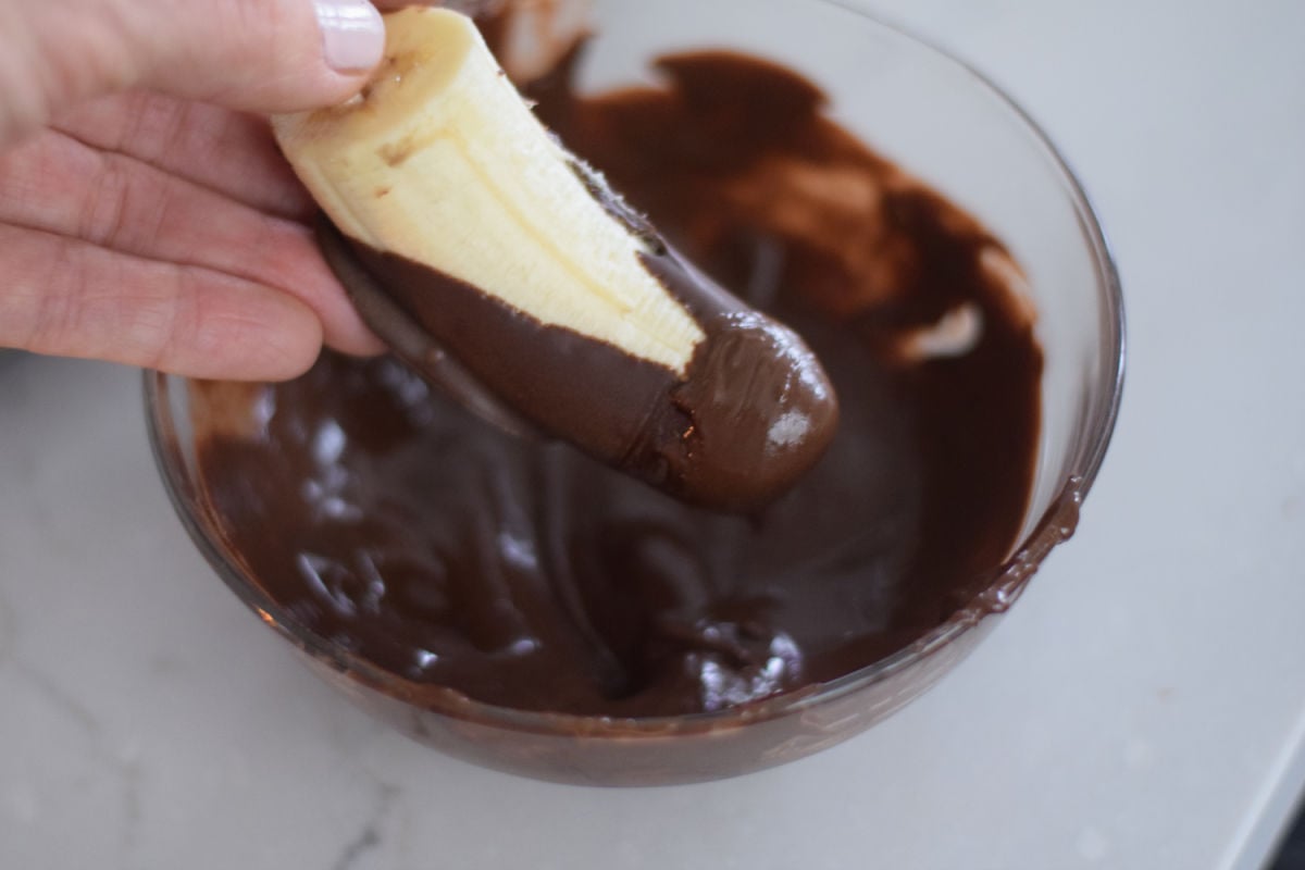 dipping frozen banana into chocolate