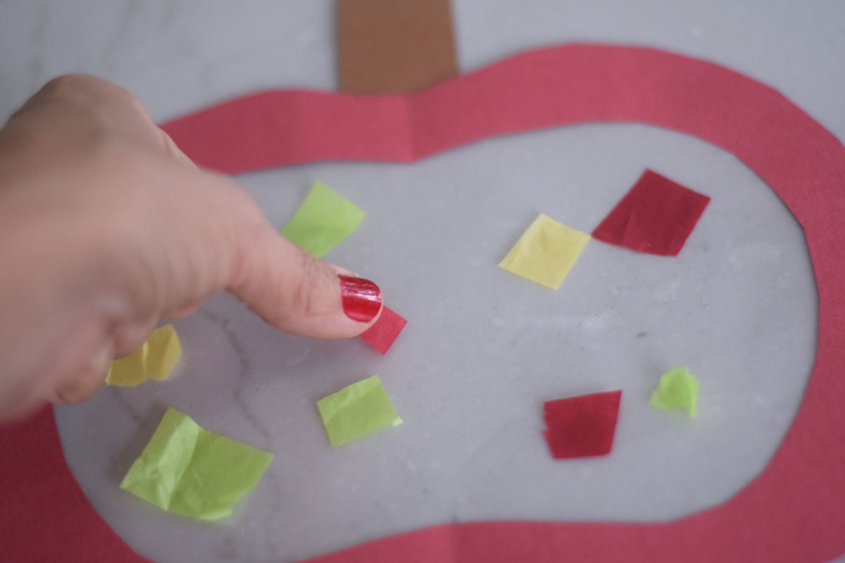 adding tissue paper to suncatcher apple craft 