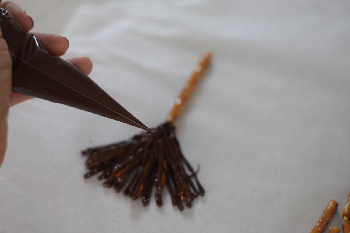 piping chocolate onto pretzel broomsticks 