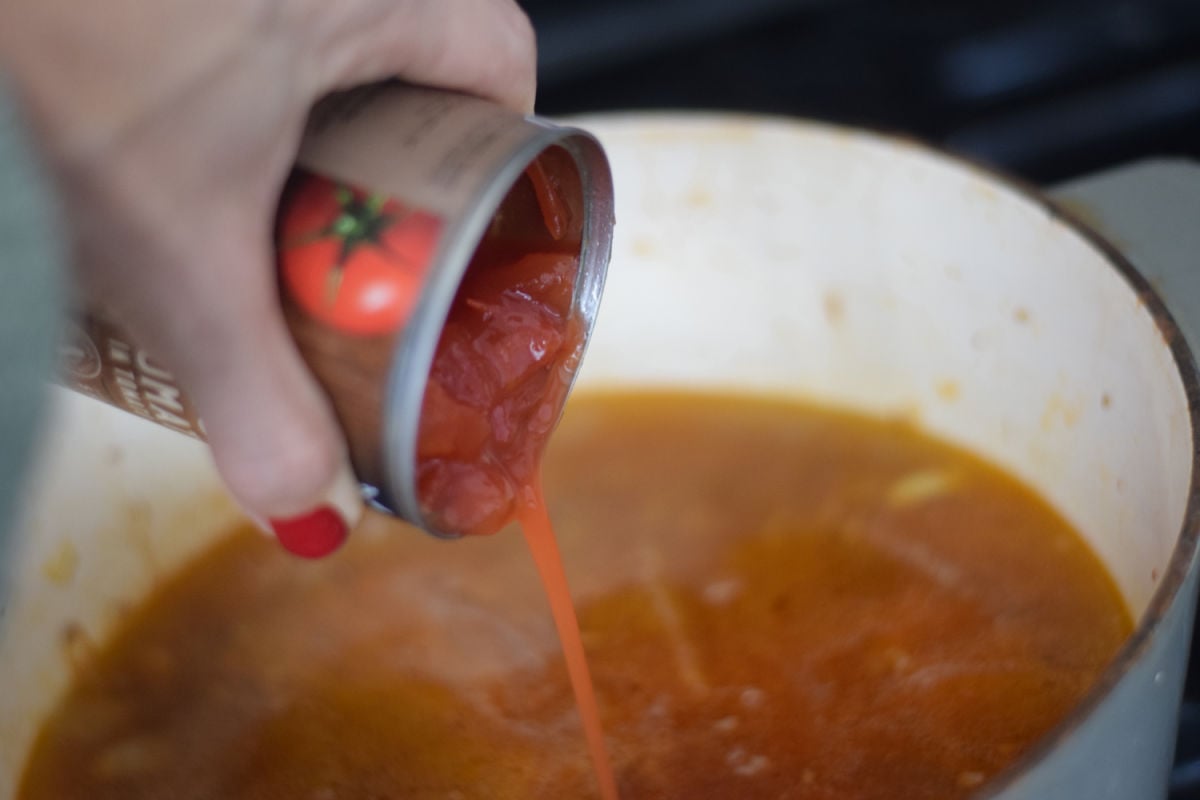 adding tomatoes to sausage soup