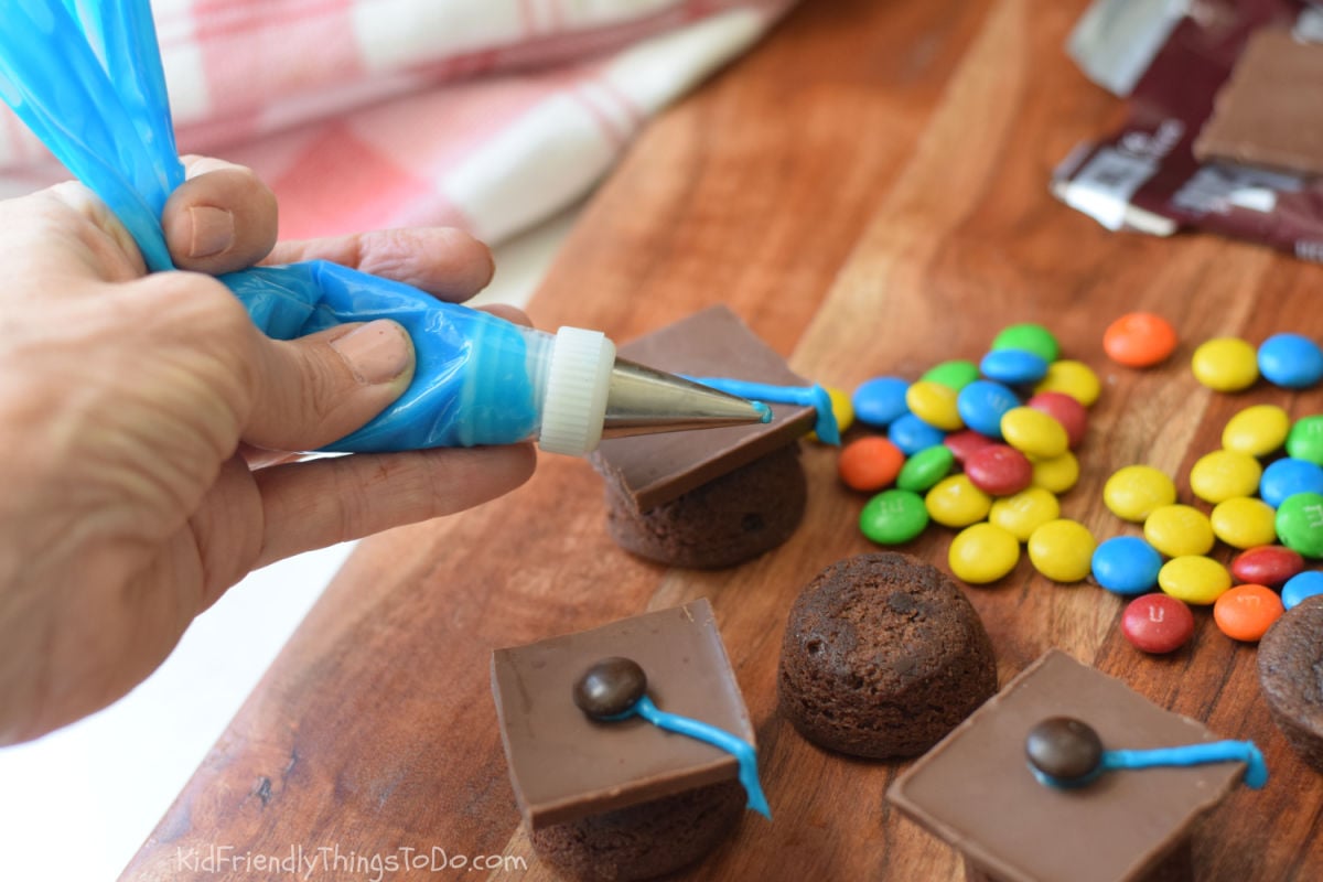 adding icing to brownie bite graduation caps 