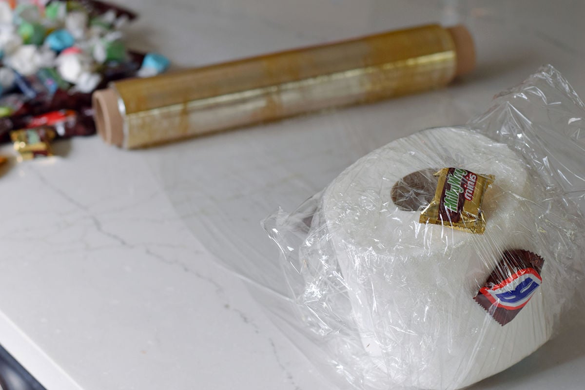 Wrapped candy and a coin placed against the toilet paper base of a saran wrap ball game.