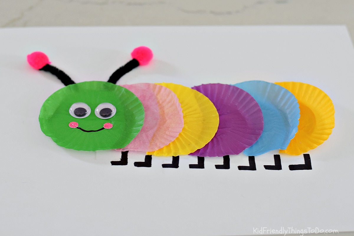 Colorful cupcake wrapper caterpillar craft made with mini cupcake liners, googly eyes, pipe cleaner antennae, and pom-poms on white cardstock.