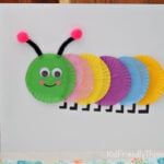 Colorful cupcake wrapper caterpillar craft made with mini cupcake liners, googly eyes, pipe cleaner antennae, and pom-poms on white cardstock.