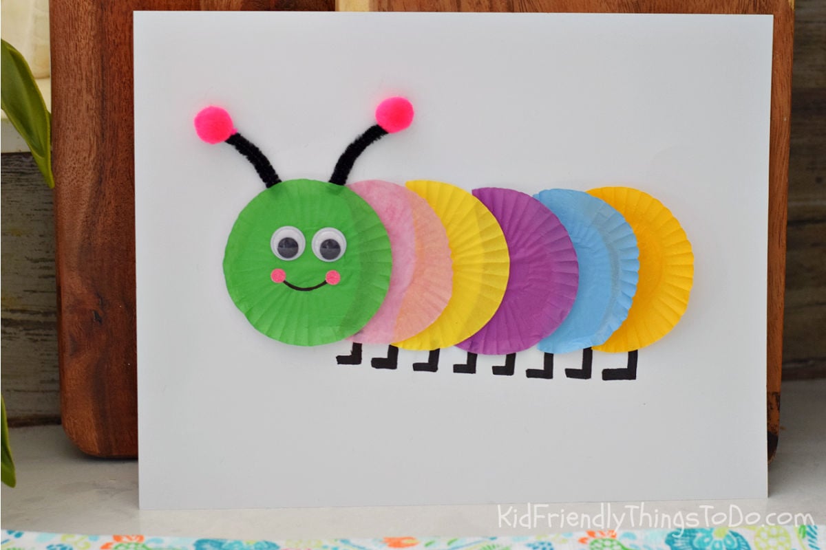 Colorful cupcake wrapper caterpillar craft made with mini cupcake liners, googly eyes, pipe cleaner antennae, and pom-poms on white cardstock.