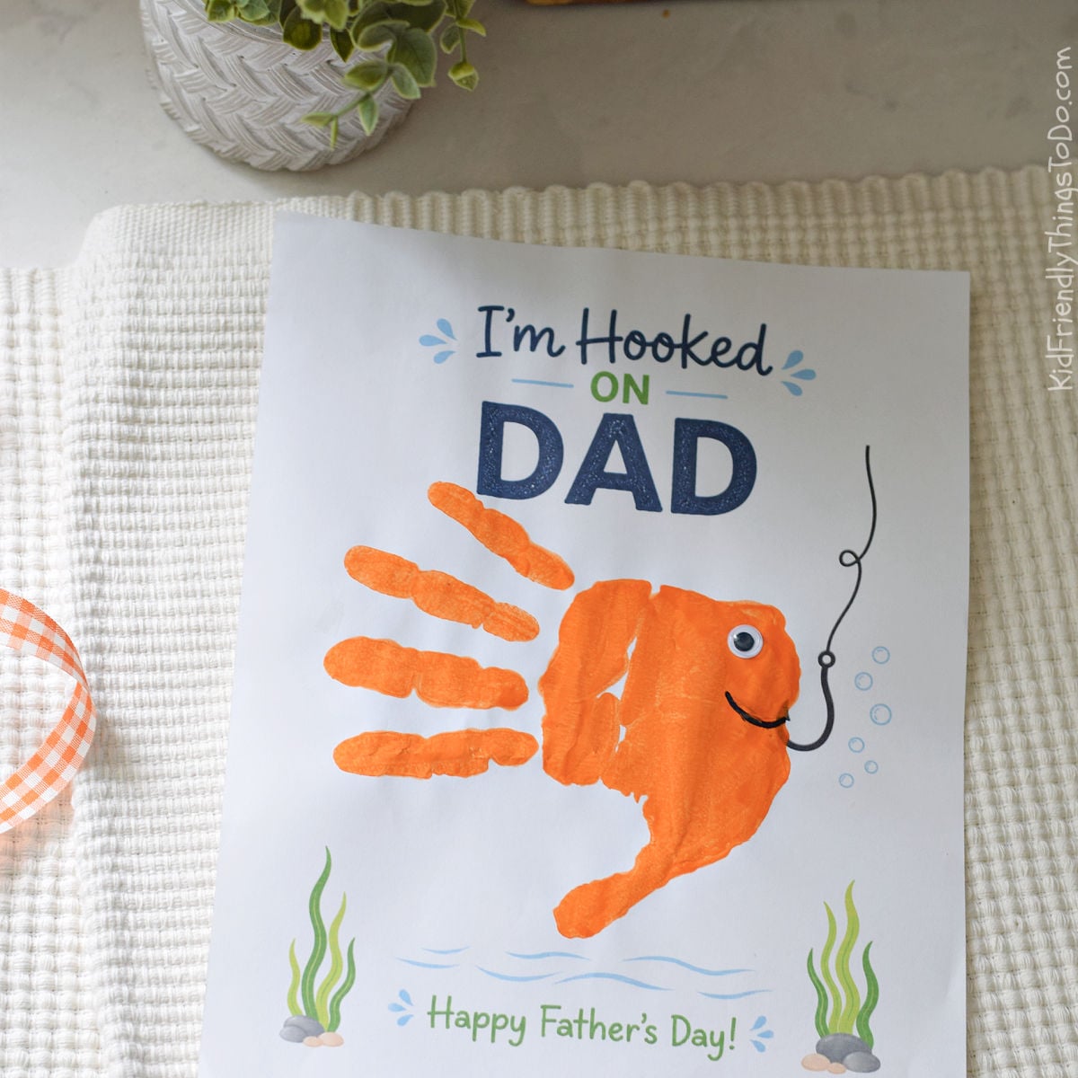 Child’s orange fish handprint craft on an “I’m Hooked on Dad” Father’s Day printable with fishing hook and ocean theme.