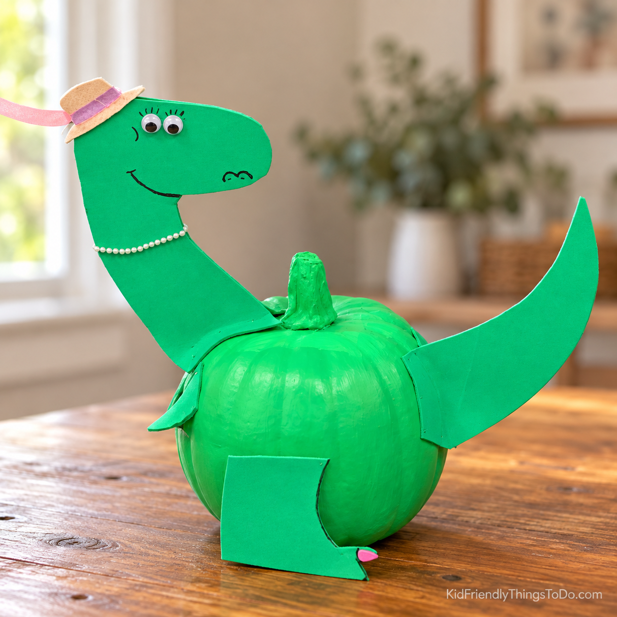 Green Edwina dinosaur pumpkin with a long neck and raised tail, googly eyes, a small hat, and a pearl necklace.