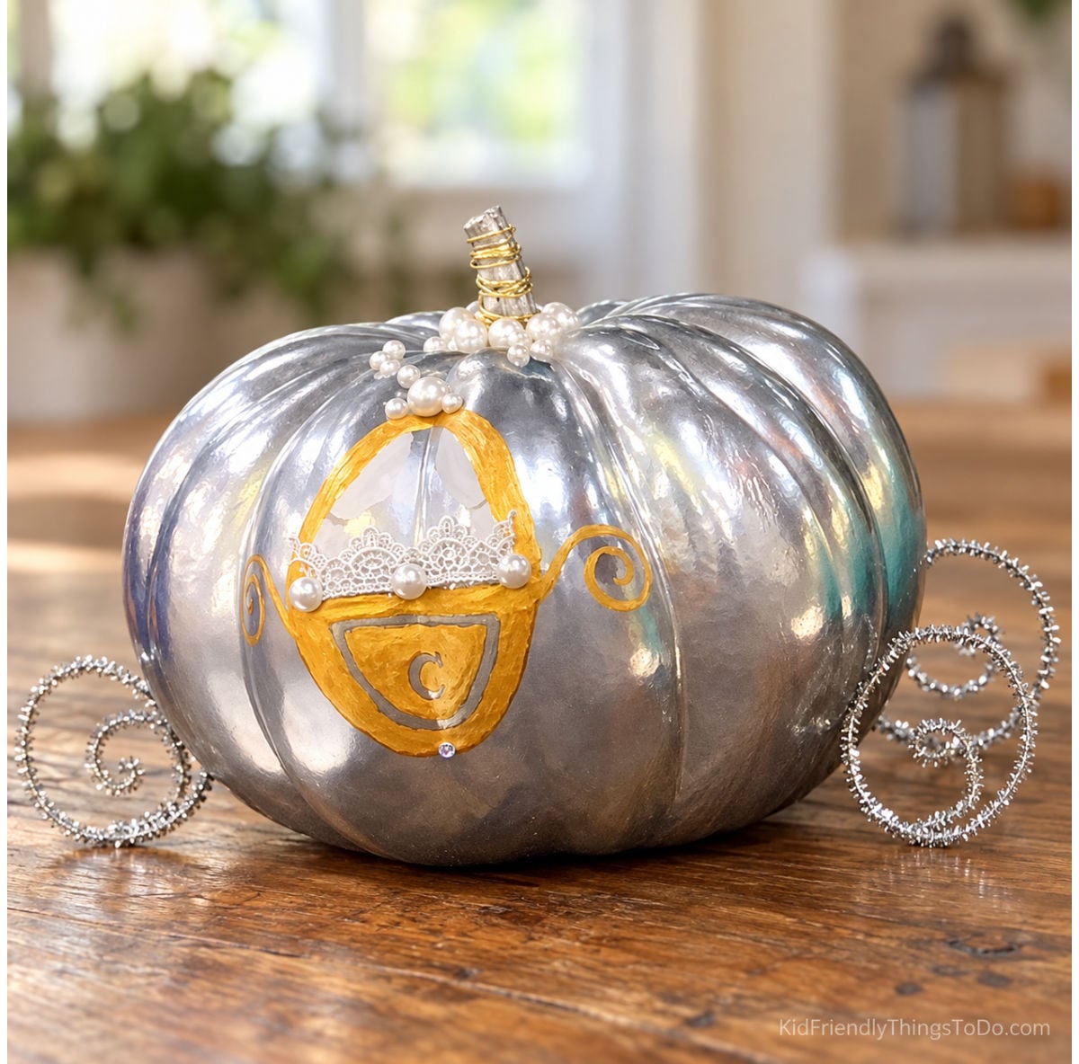 Silver Cinderella carriage pumpkin with gold painted details, pearl beads, a small tiara, and curled silver pipe-cleaner wheels.