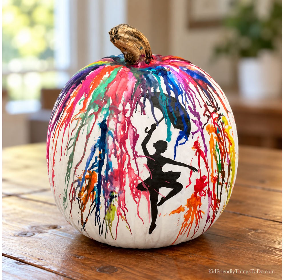 White no-carve pumpkin decorated with colorful dripping streaks and a black ballerina silhouette, displayed on a wooden table.