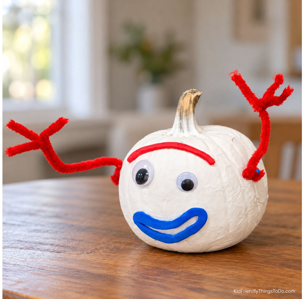 White no-carve Forky pumpkin with mismatched googly eyes, a red eyebrow, blue smile, and red pipe cleaner arms.