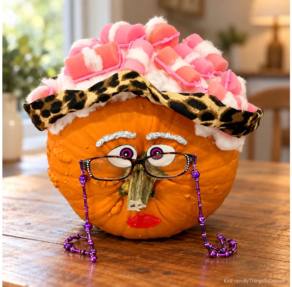 No-carve old lady pumpkin with pink hair rollers, white hair, leopard-print headband, glasses with a purple beaded chain, and a stem nose.