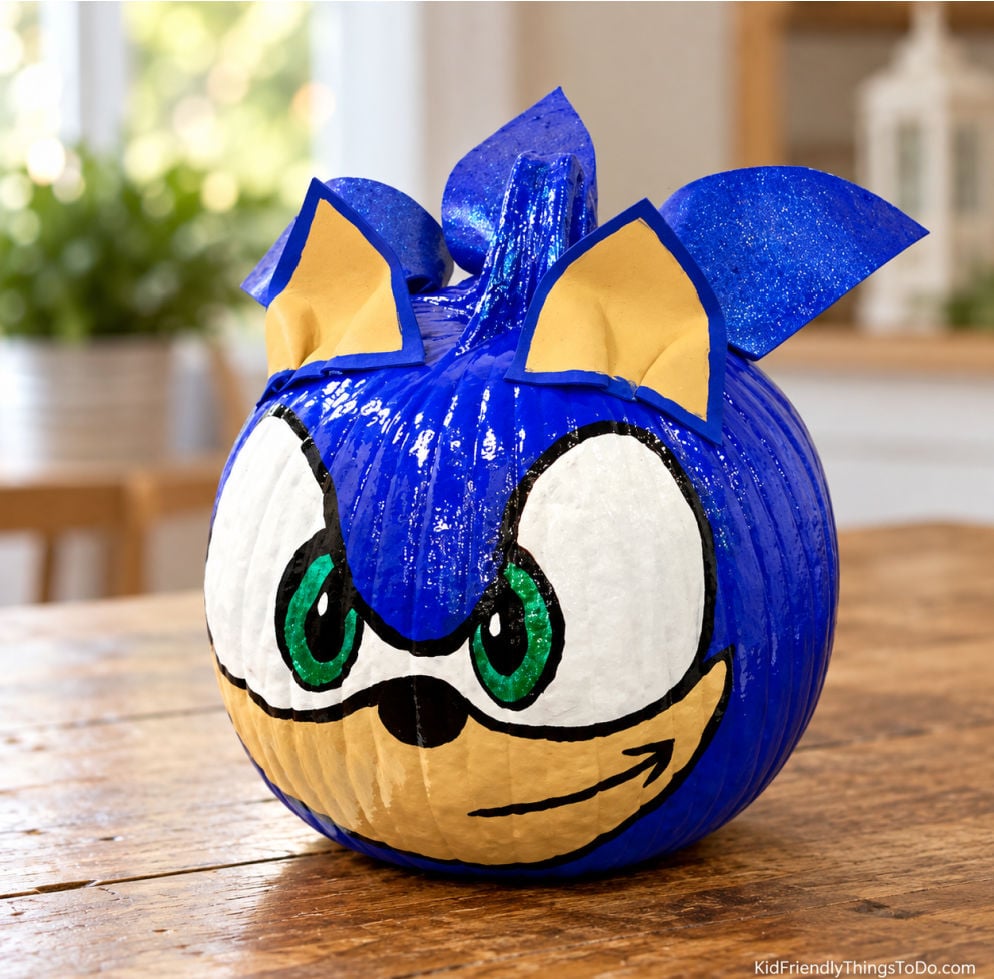 Blue no-carve Sonic the Hedgehog pumpkin with green eyes, pointed ears, and a painted smile on a wooden table.