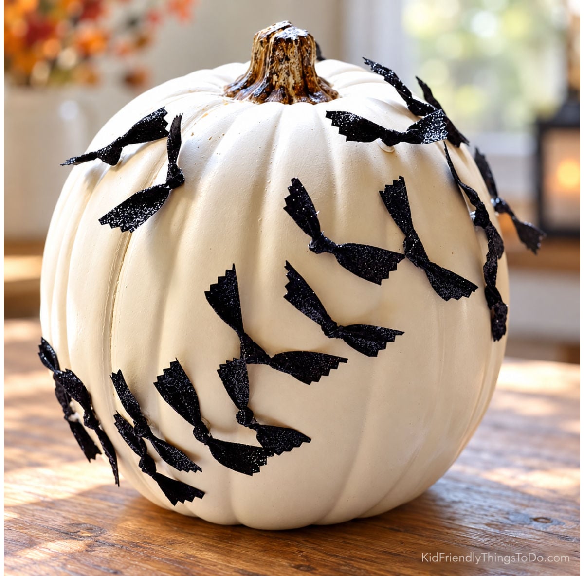 White no-carve pumpkin decorated with a diagonal swarm of black glitter ribbon bats.
