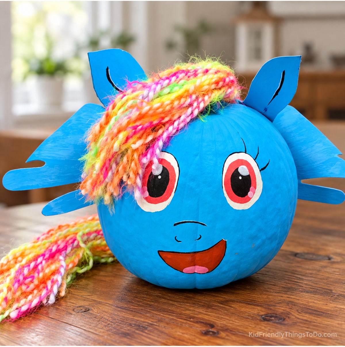 Blue My Little Pony pumpkin with a rainbow yarn mane and tail, blue wings and ears, and a hand-painted smiling face.