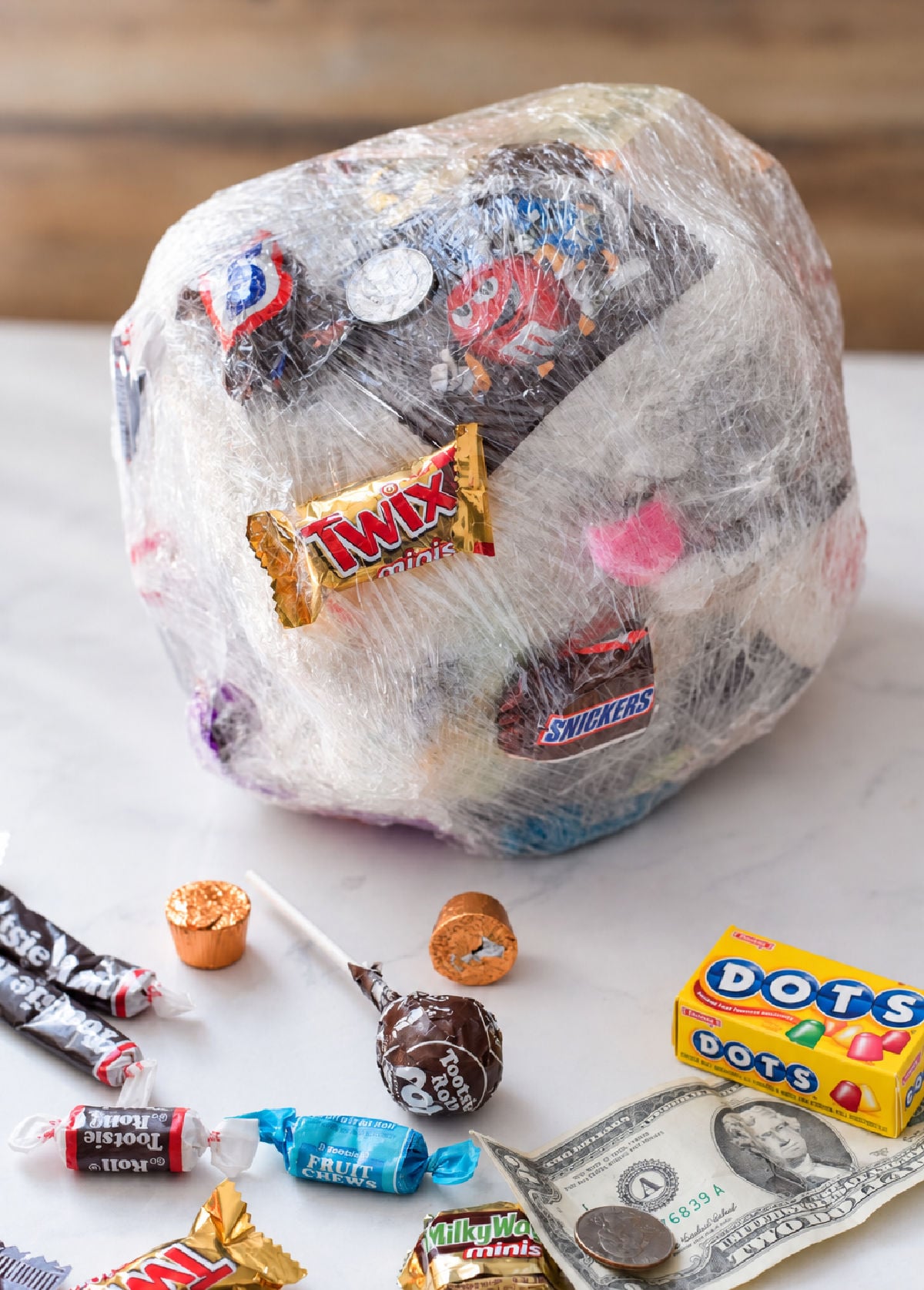 Saran wrap ball game filled with candy and coins, with wrapped treats and a five-dollar bill on the table.