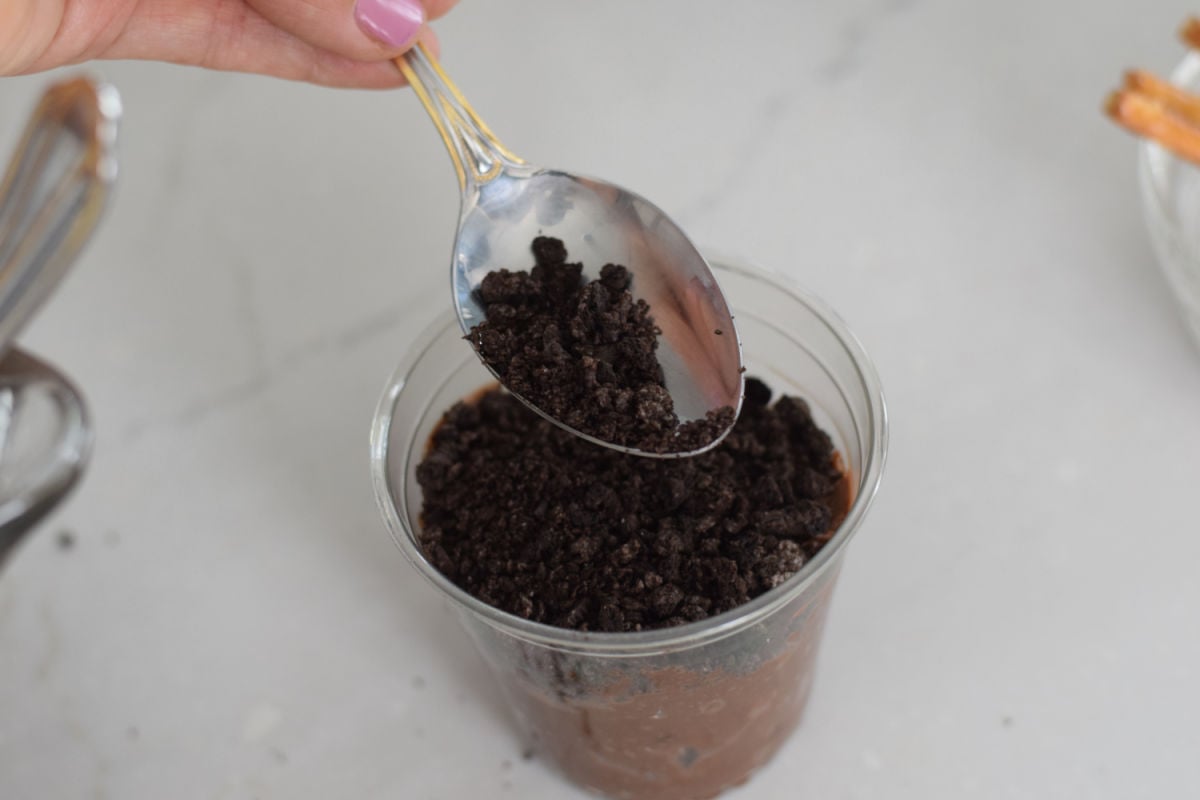 spooning crushed Oreo cookies over pudding for campfire dirt cups