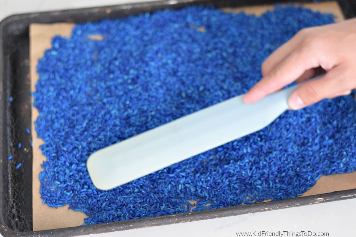 spreading out blue colored rice for a minion jar craft 