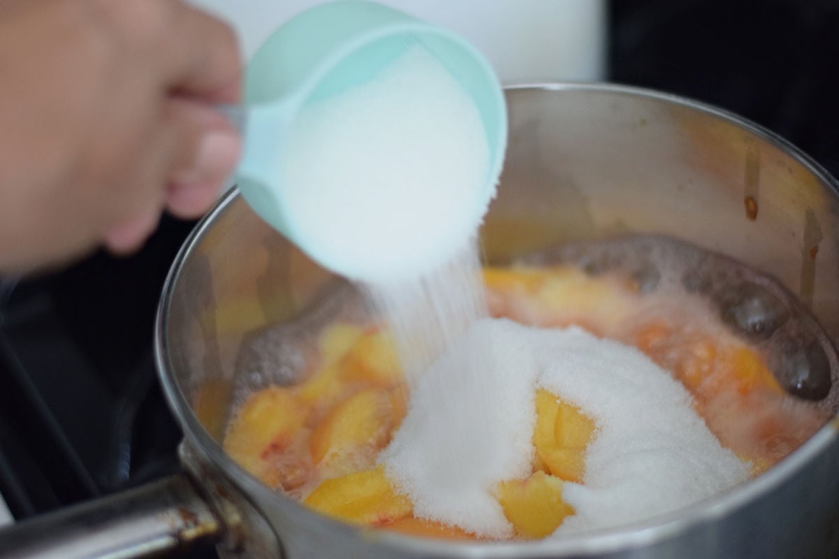 adding sugar to fresh peaches as they cook to form syrup